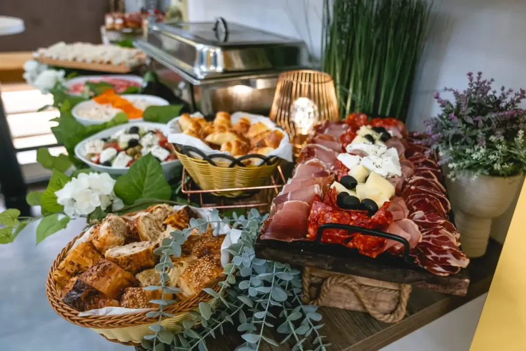 Švedski sto za roditelje sa keteringom koji je ukrašen veštačkim cvećem i zelenilom. U ponudi je: bogato predjelo,